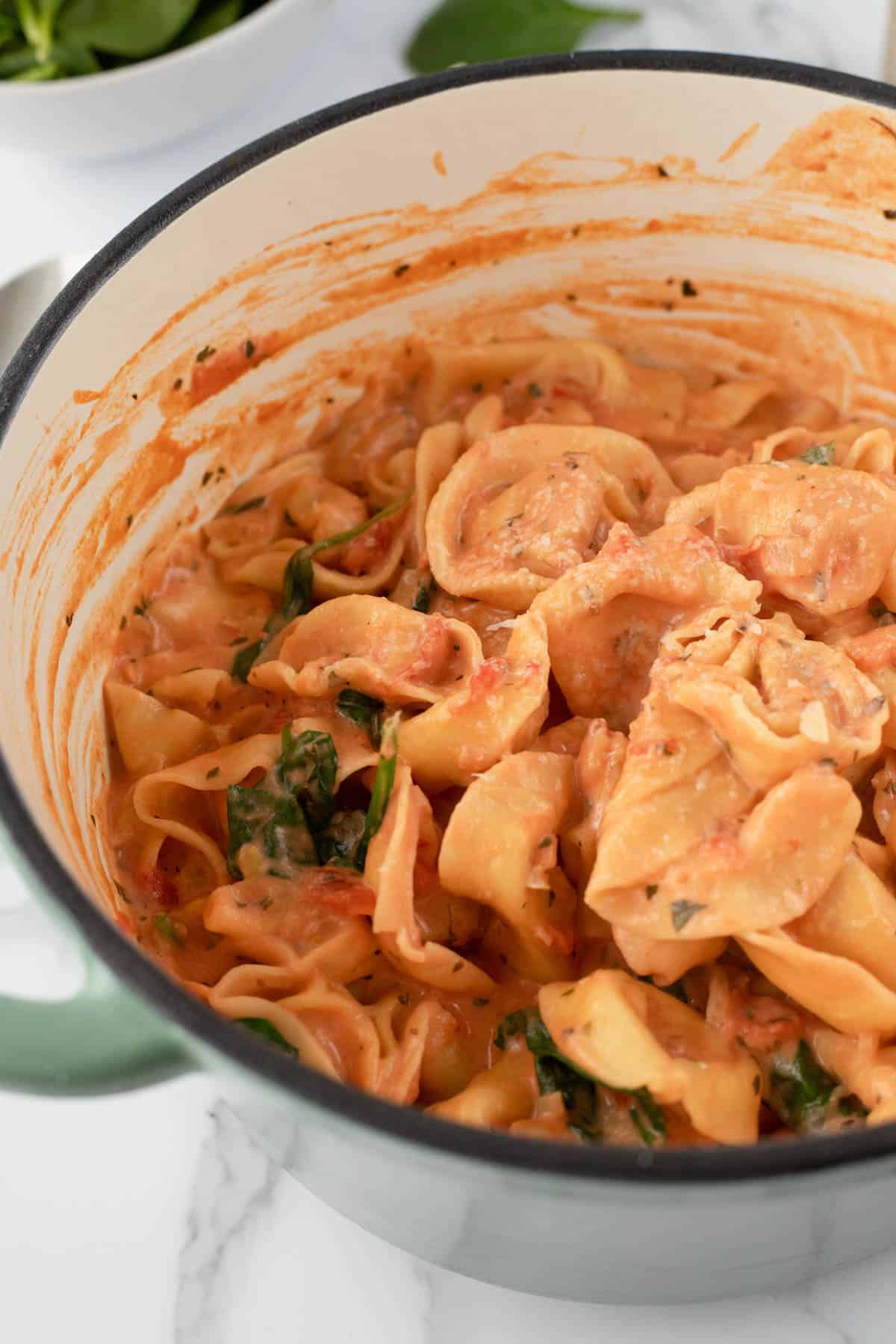 Tortellini pasta in pink sauce with spinach in a large pot.