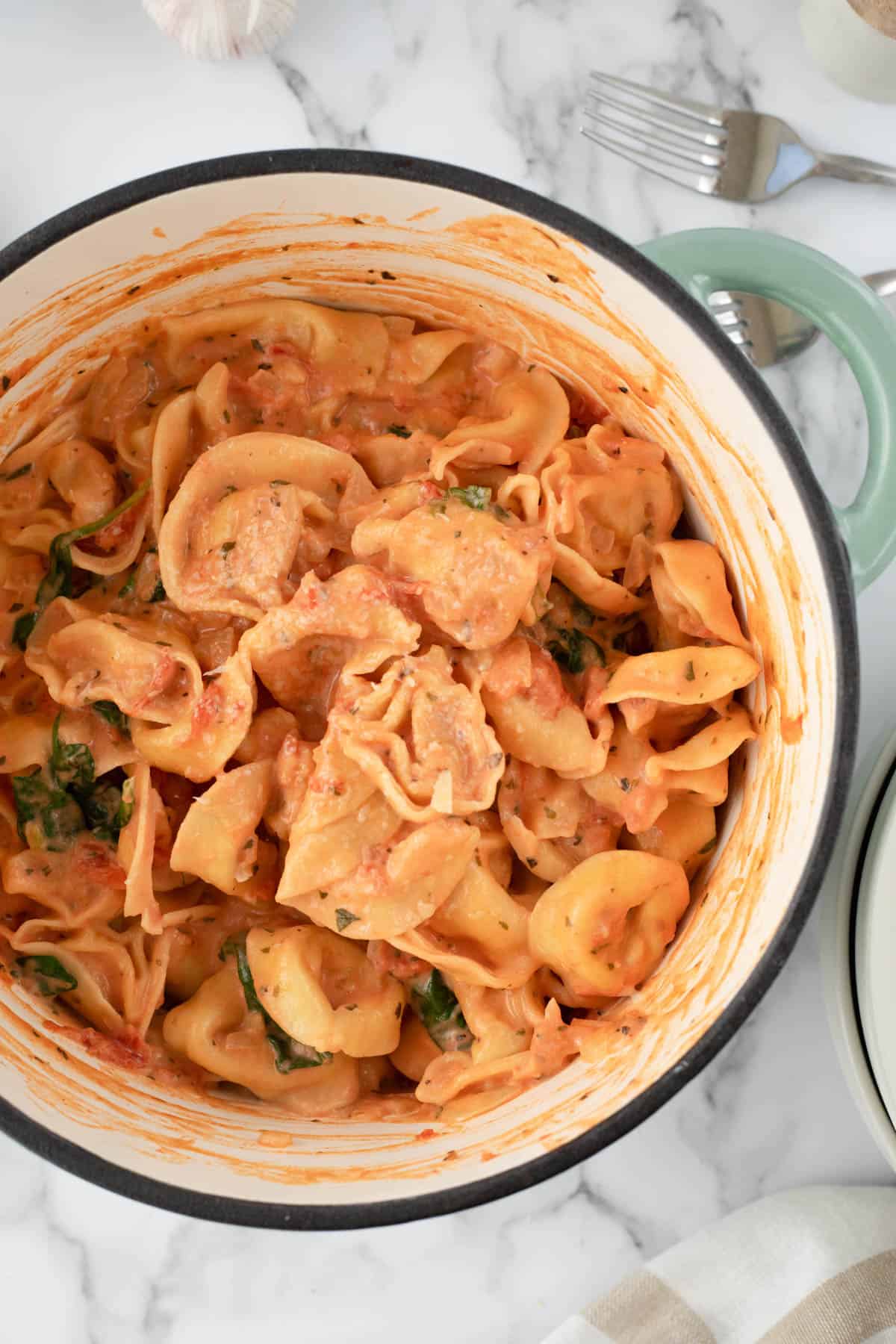 An overhead image of a pot filled with creamy tomato and spinach tortellini pasta.