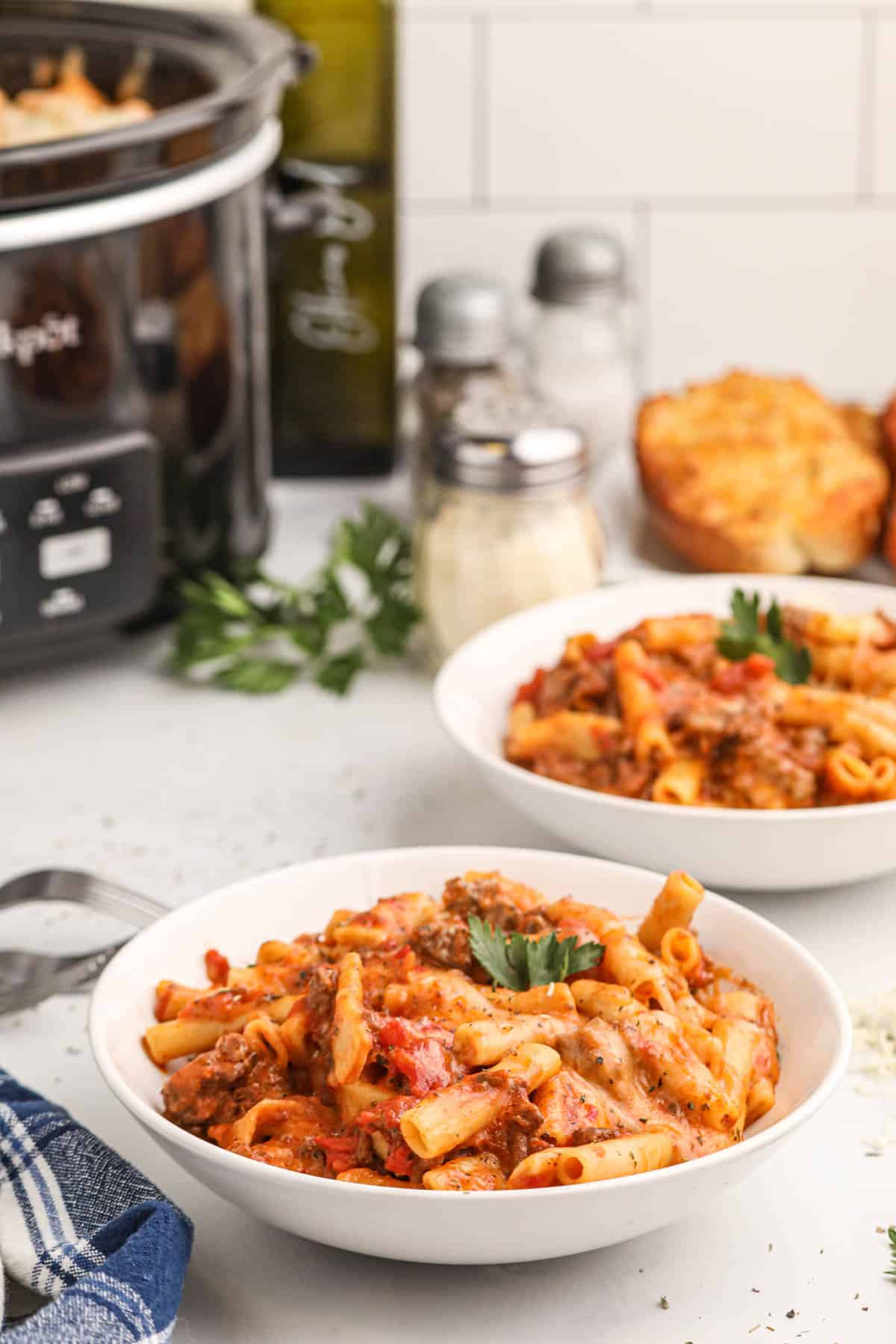 Bowls of baked ziti pasta in front of a slow cooker.