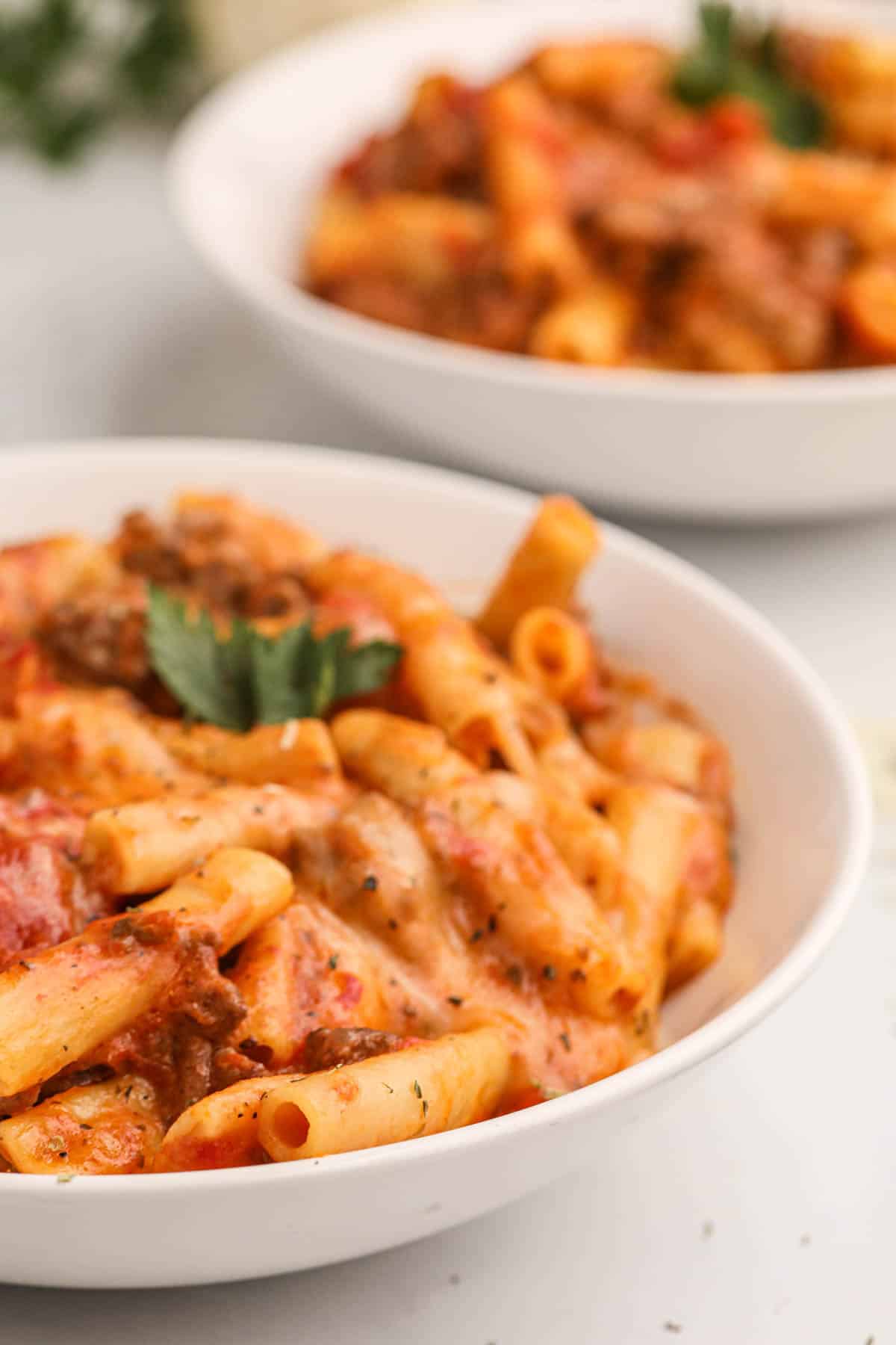 A close image of cheesy baked ziti in a white pasta bowl.