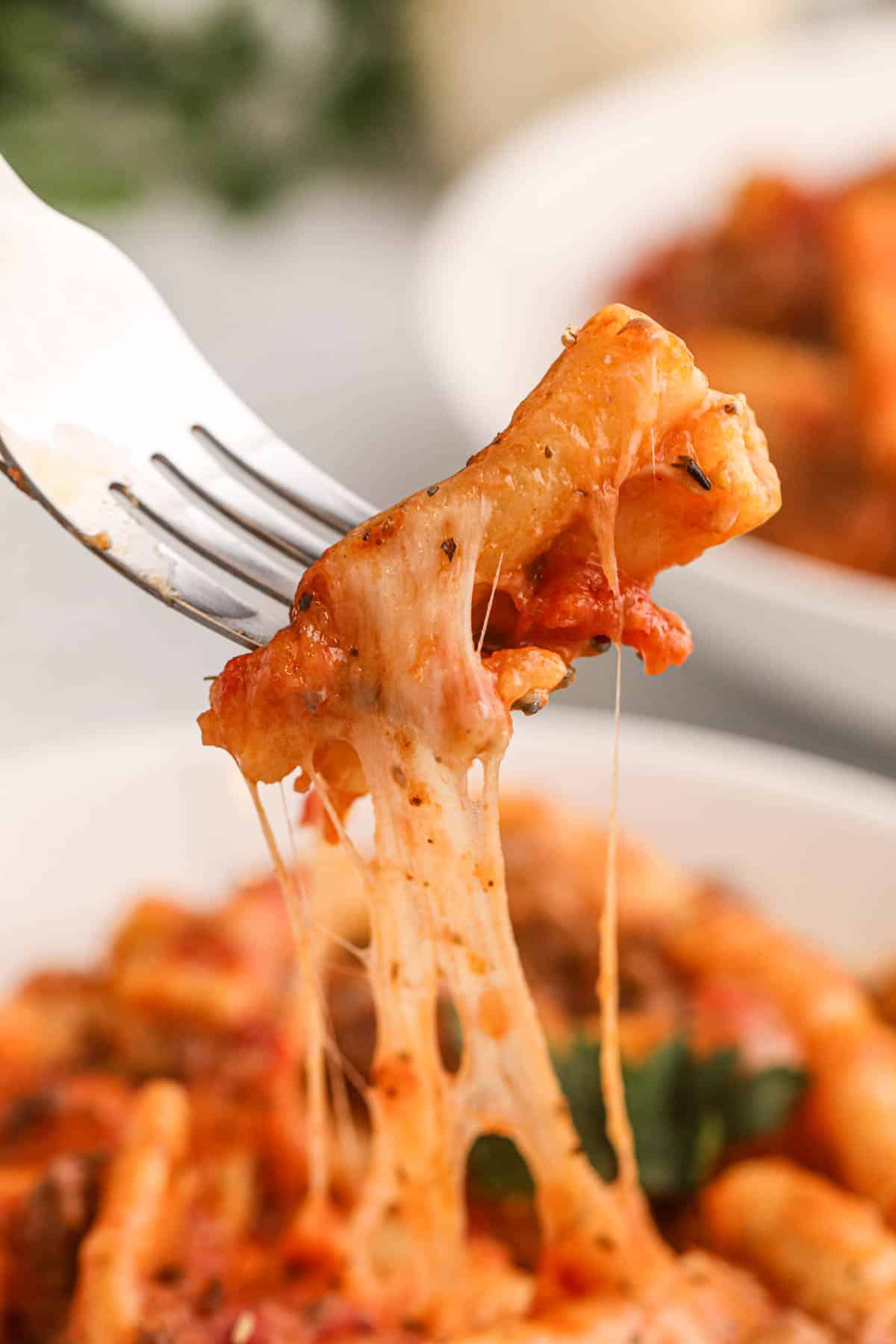 A fork lifting a bite of crock pot baked ziti pasta with cheese stretching off of it.