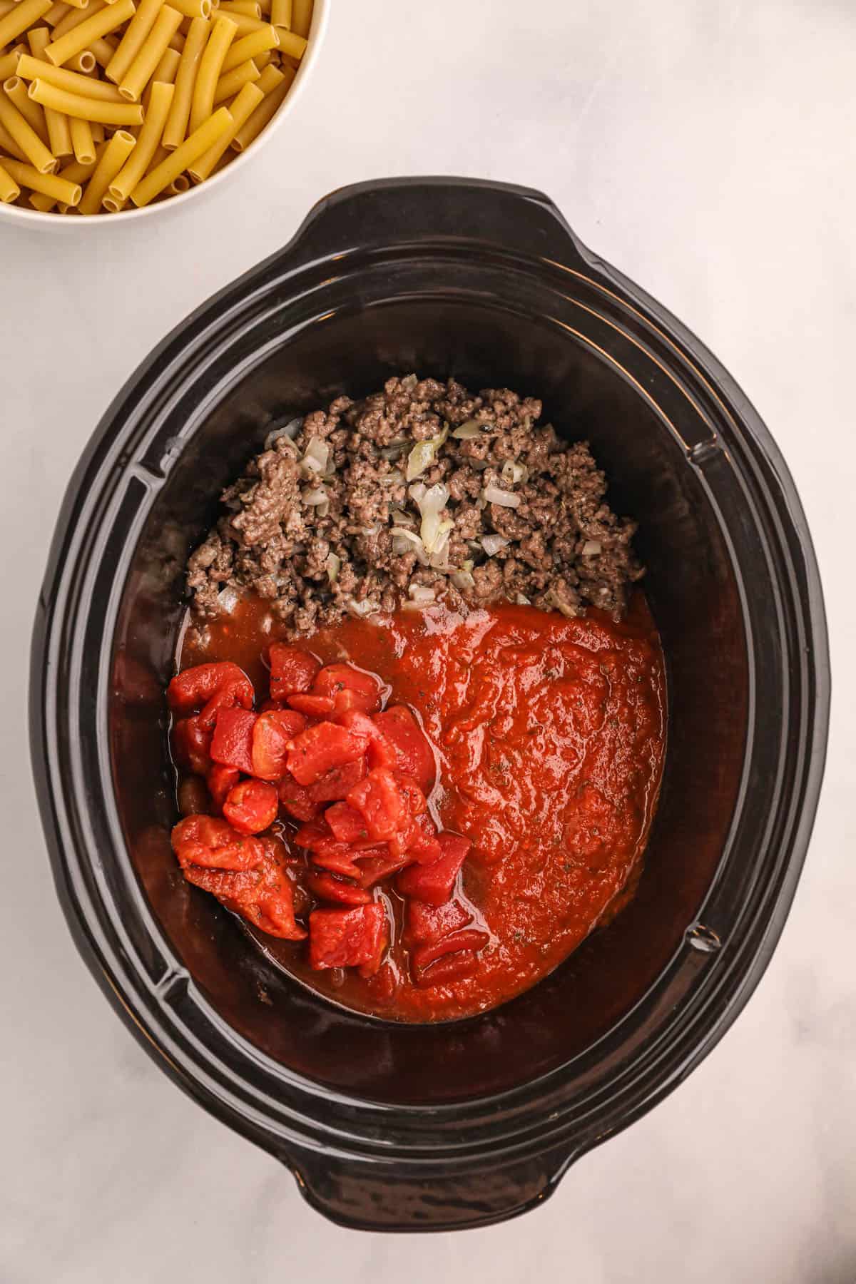 Adding tomato pasta, marinara sauce, and cooked ground beef to a crock pot.
