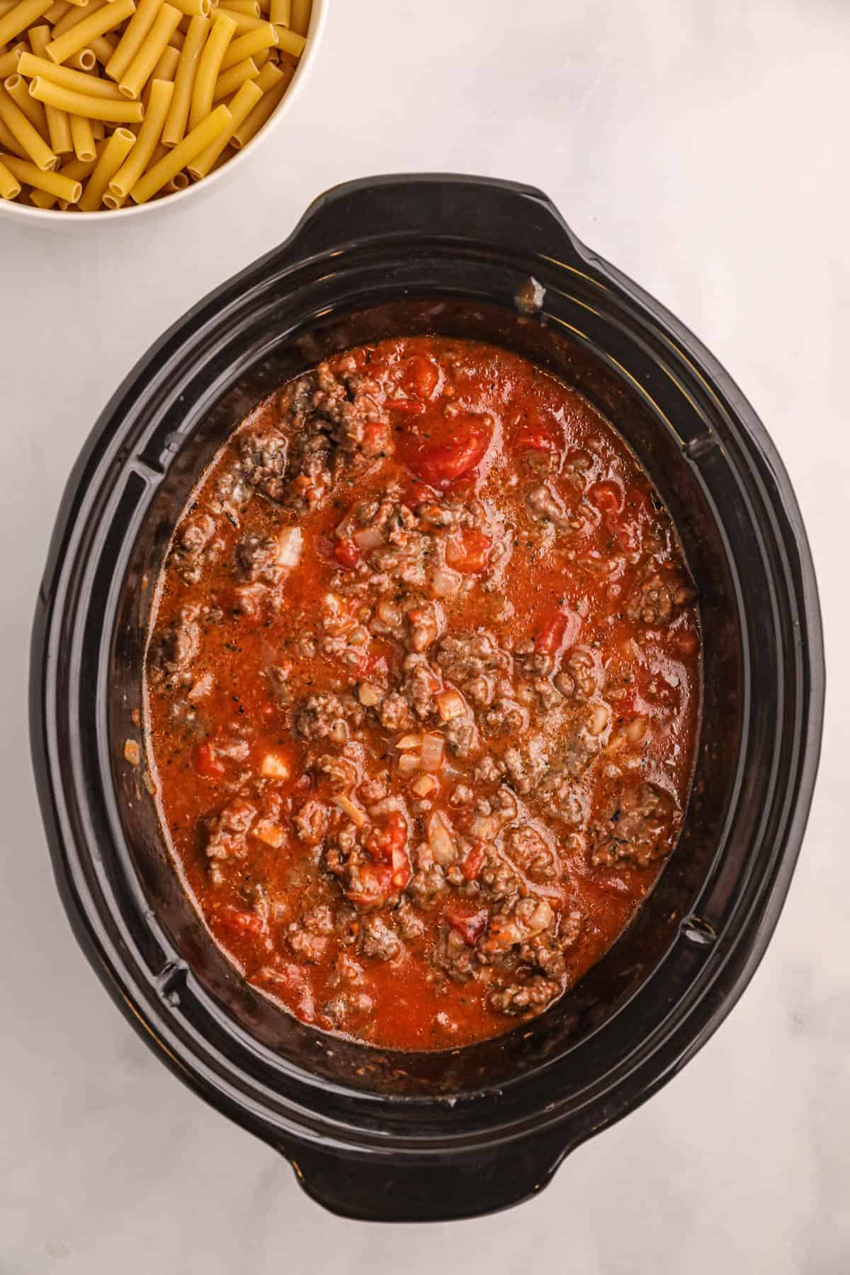 A large black crock pot with marinara sauce and cooked ground beef.