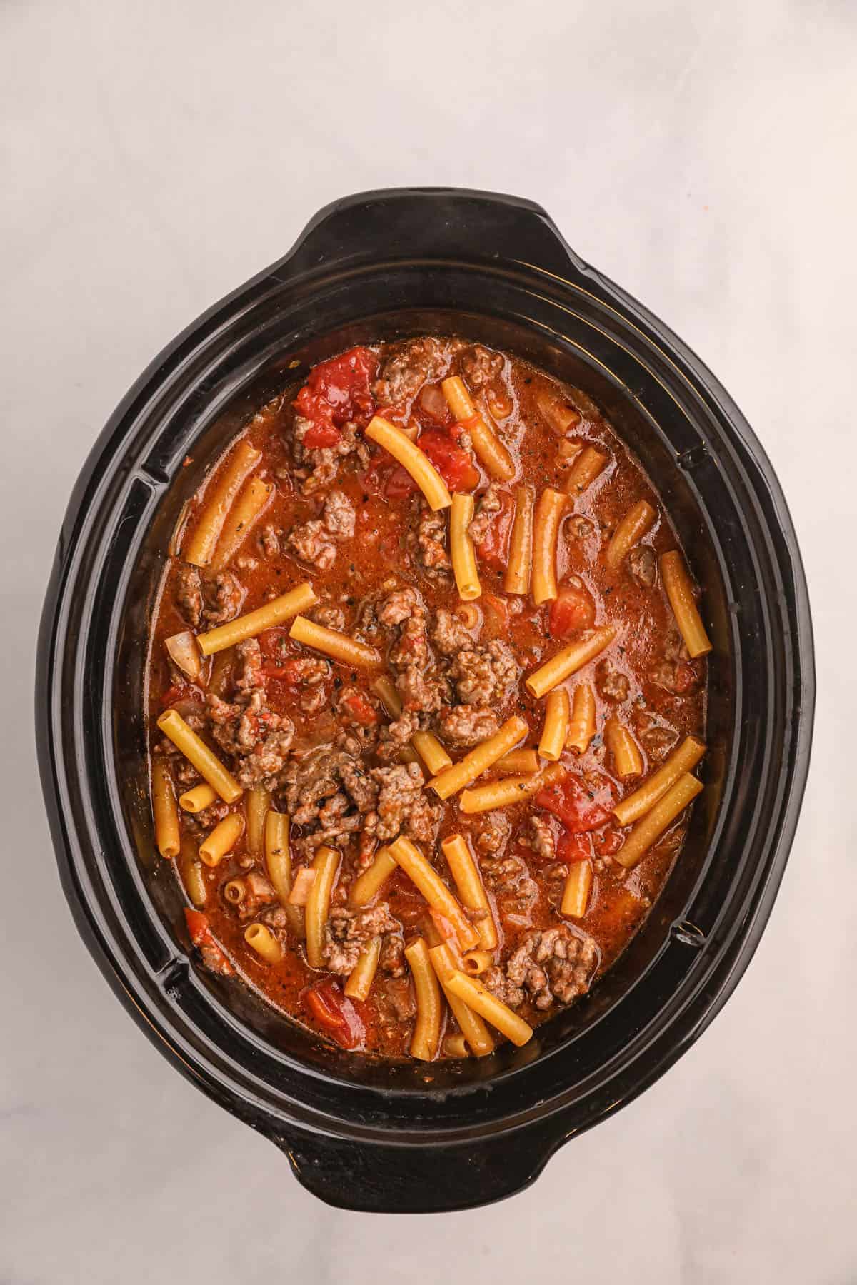 Adding uncooked ziti noodles to the crockpot with browned meat anad tomato sauce.