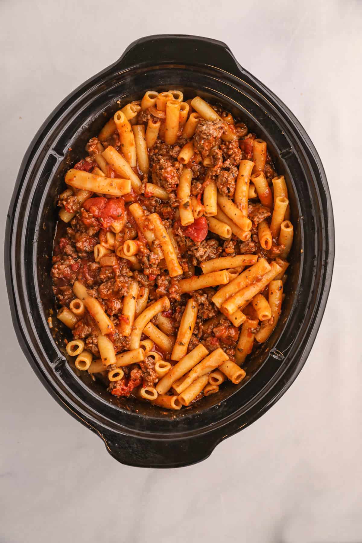 Cooked ziti pasta, meat, and sauce in a large black crock pot.