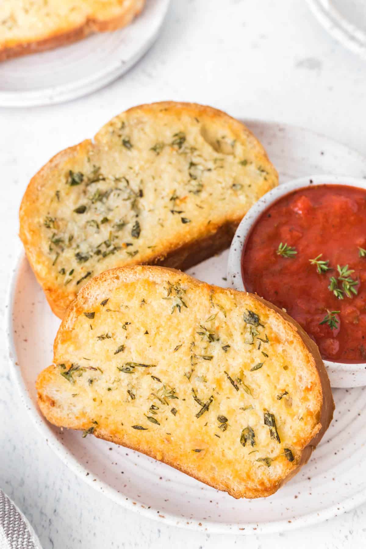 Garlic bread on a plate with a bowl of marinara sauce.