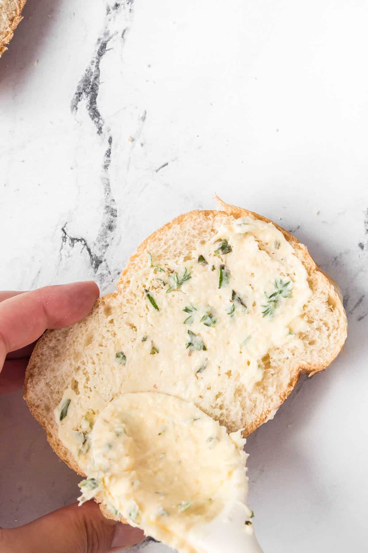 Spreading garlic butter spread onto a slice of Italian bread.
