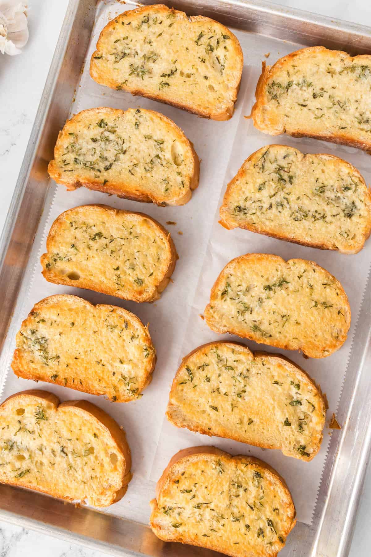 Pieces of homemade garlic bread in rows on a baking sheet.