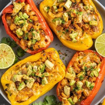 Red and yellow stuffed bell peppers on a plate with cilantro and lime.