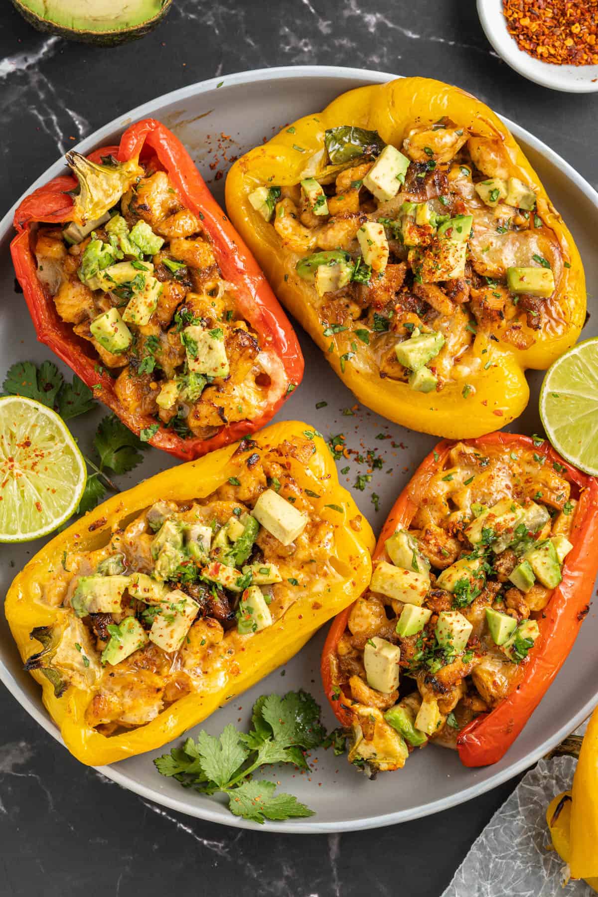 Red and yellow stuffed bell peppers on a plate with cilantro and lime.