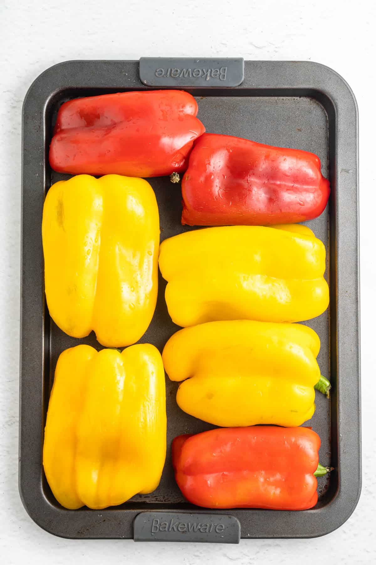 Red and yellow bell pepper halves arranged on a baking sheet.