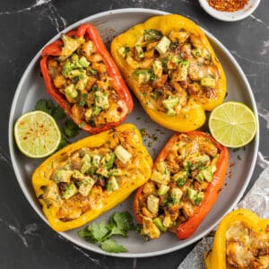 Four fajita chicken stuffed peppers on a plate with limes.