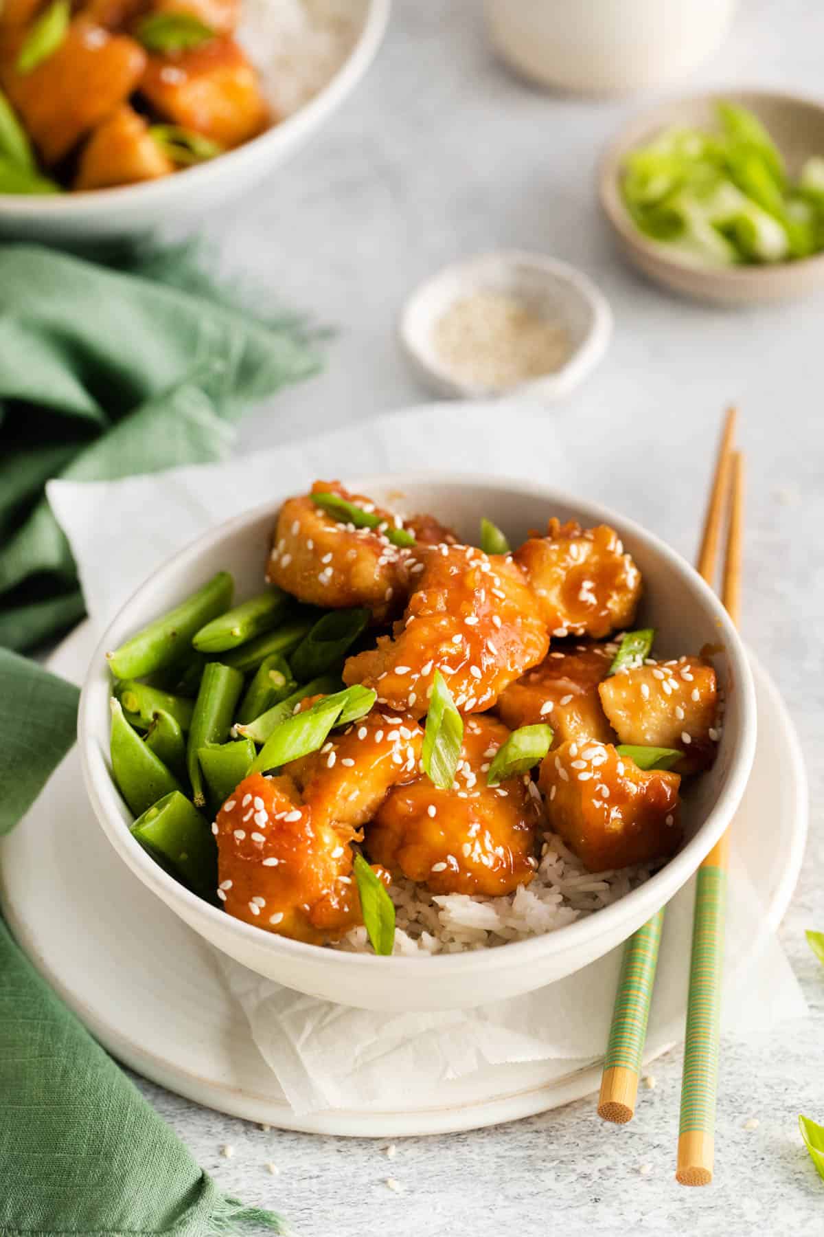A honey garlic chicken bowl with rice and sugar snap peas with chopsticks lying next to it.