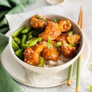 A honey garlic chicken bowl with rice and sugar snap peas with chopsticks lying next to it.