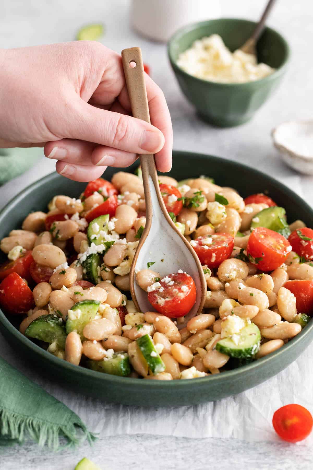 A hand holding a spoon getting a scoop of Mediterranean White Bean Salad from a plate.