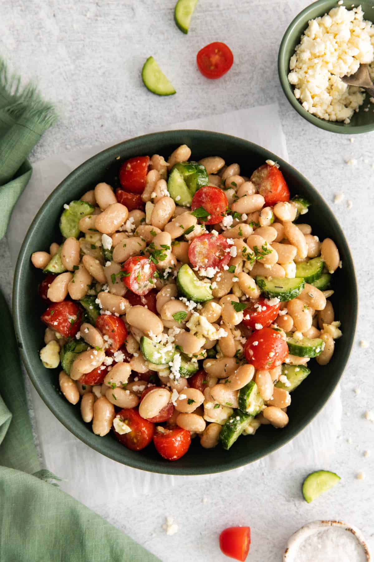 A green plate with a serving of Mediterranean white bean salad with cucumbers and tomatoes.