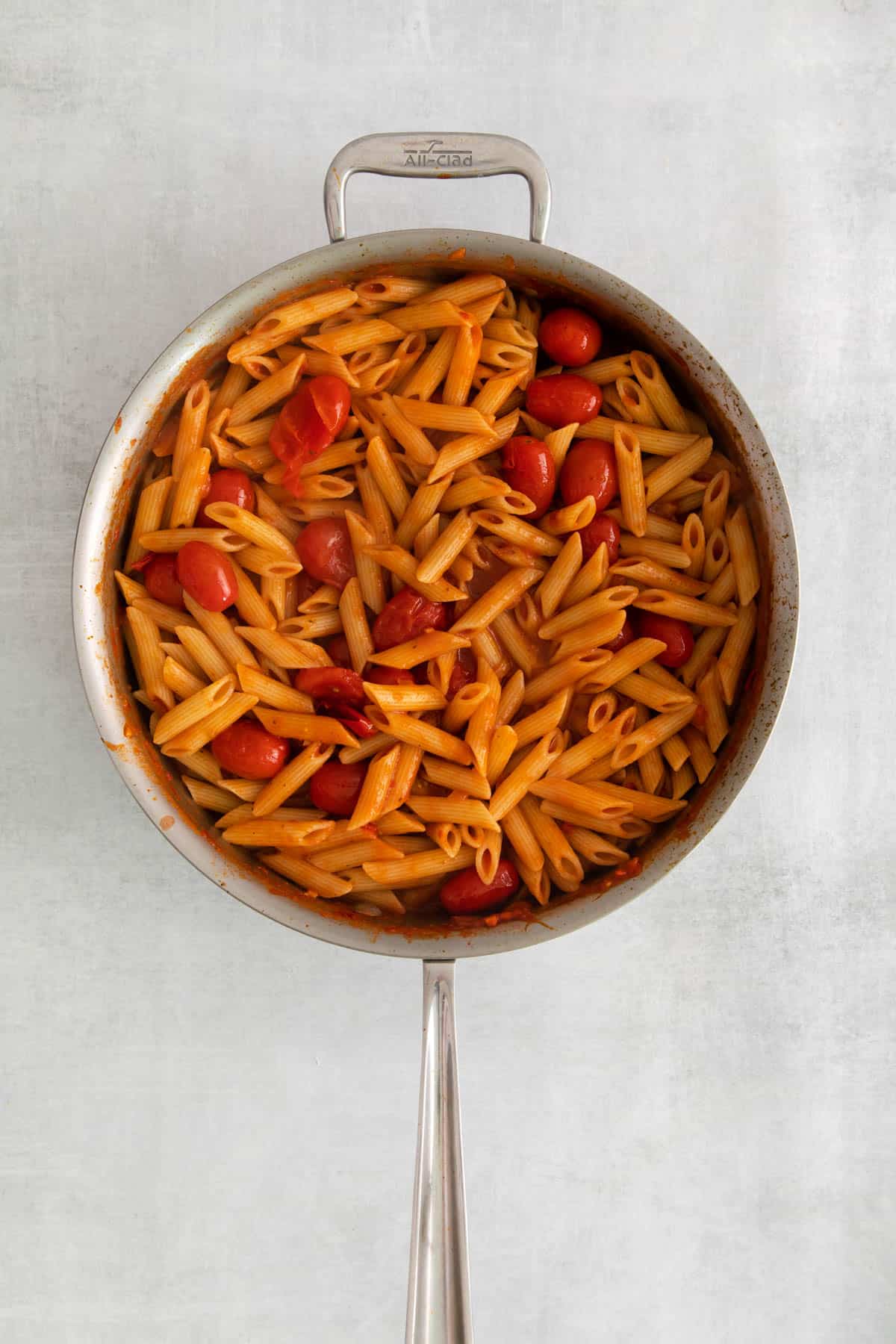 Cooked penne pasta tossed with arrabbiata sauce in a large pan.