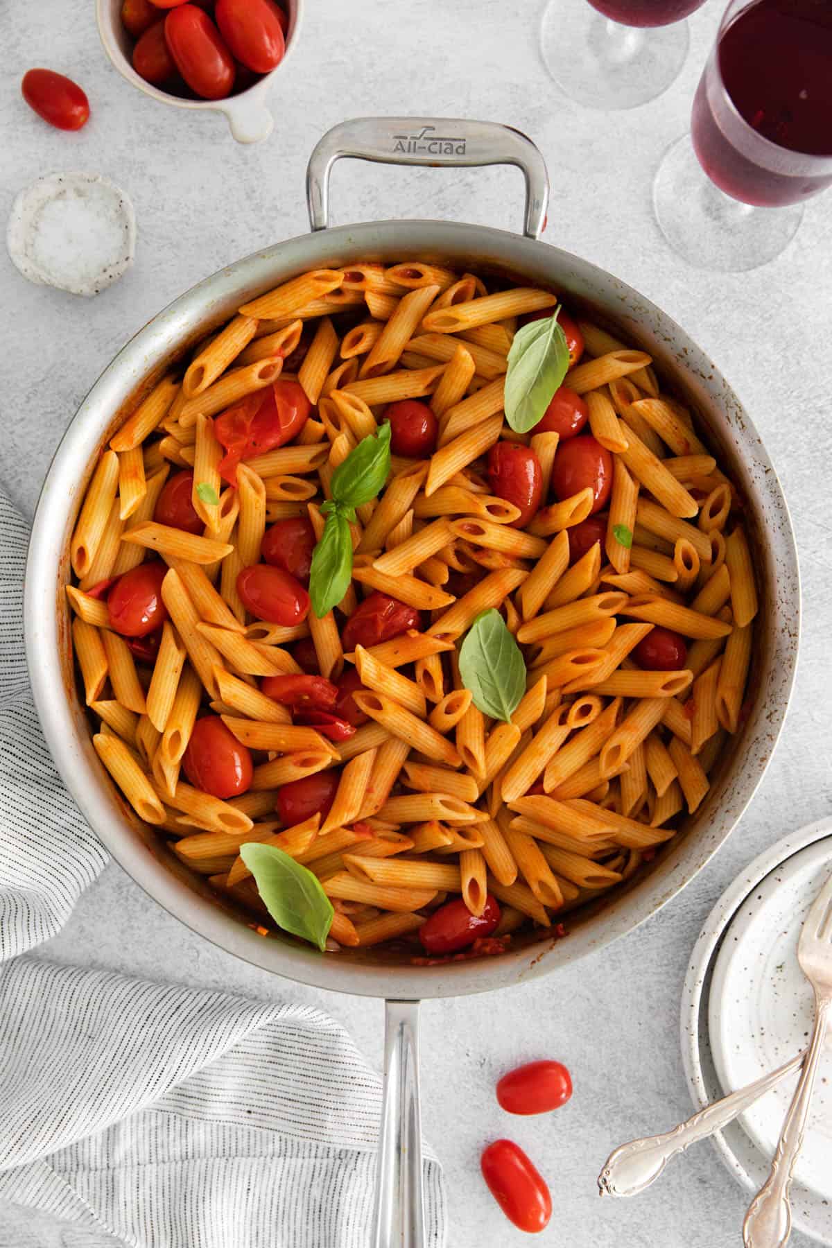 A large pan filled with penne all'arrabbiata garnished with fresh tomatoes and basil leaves.