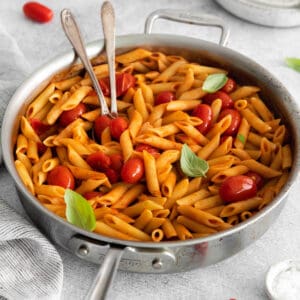Penne all'Arrabbiata in a large pan with two serving spoons.