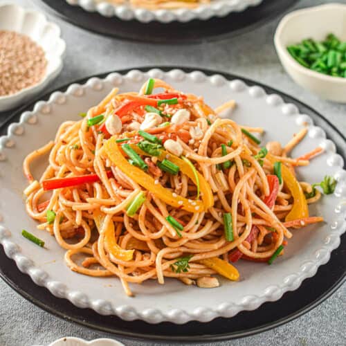 A pile of Thai peanut noodles with red and yellow bell peppers on top.