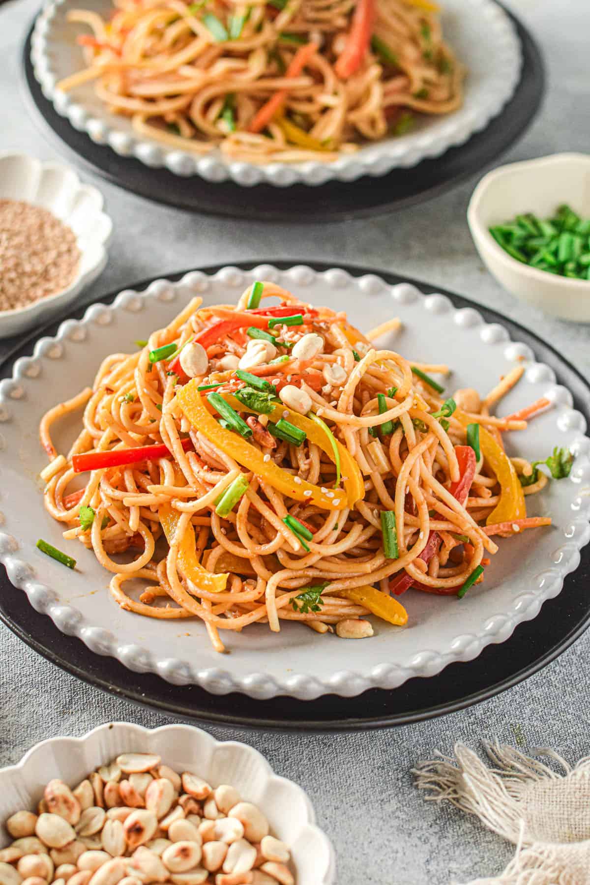 A pile of Thai peanut noodles with red and yellow bell peppers on top. 