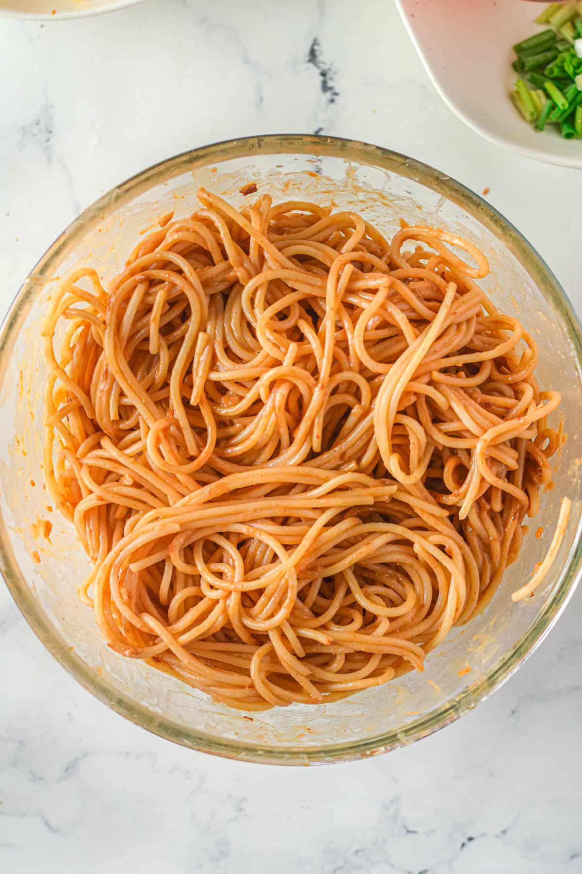 Cooked spaghetti pasta tossed with Thai peanut sauce in a large bowl.