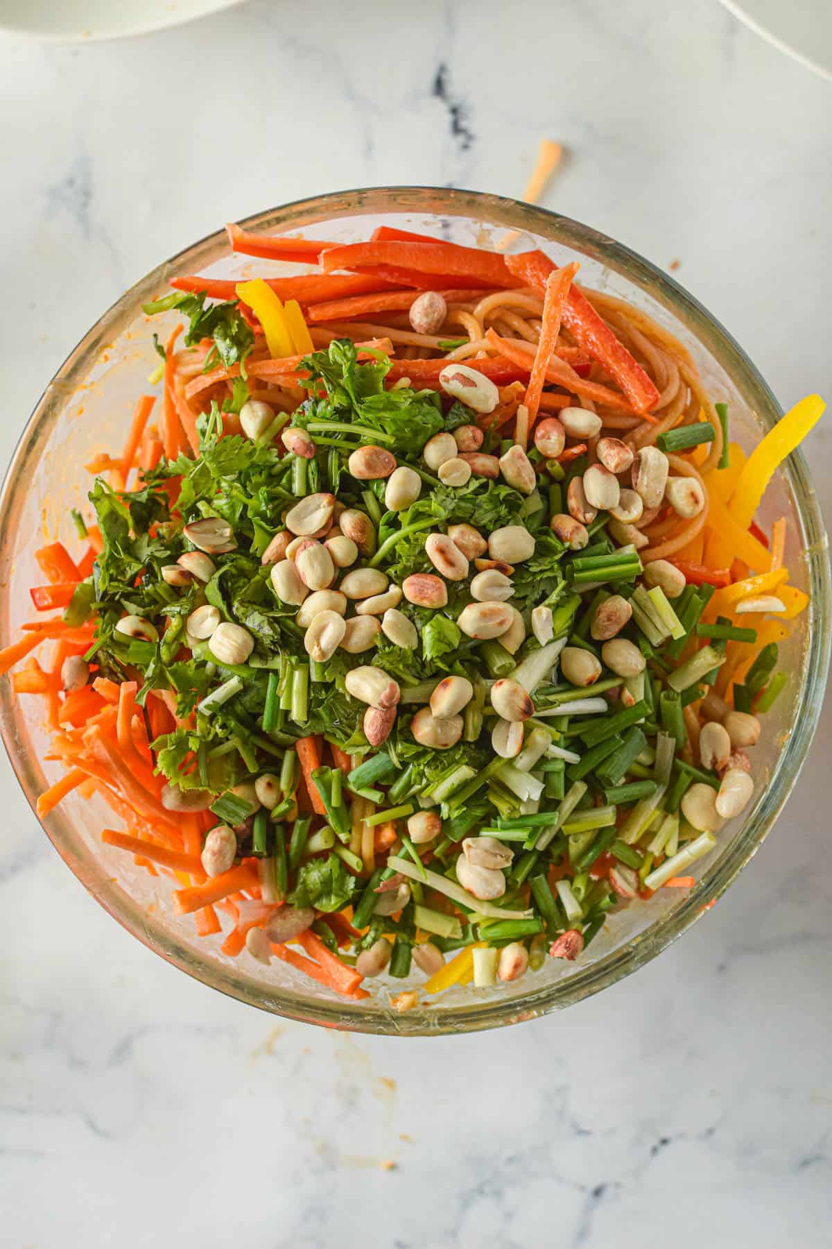Adding chopped peanuts and green onions to a large bowl with vegetables and cooked pasta.