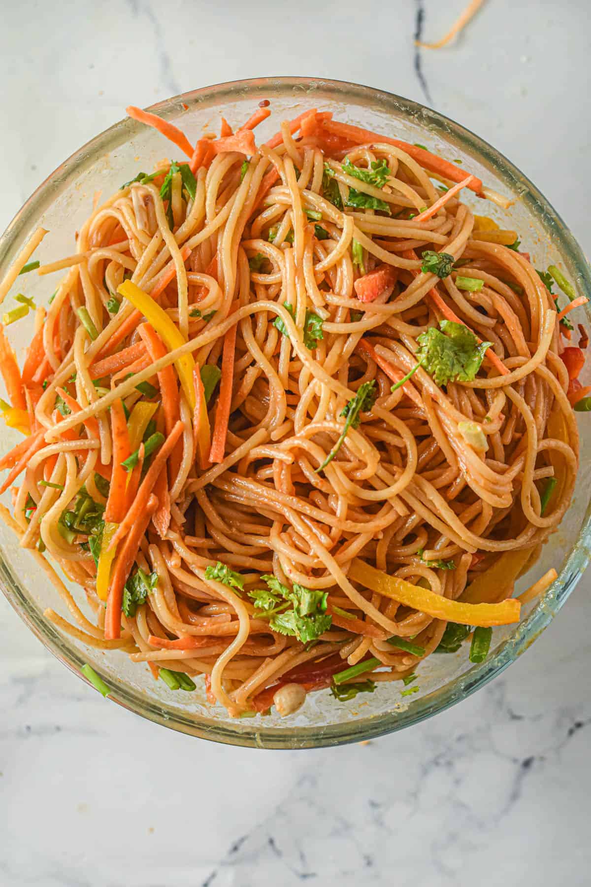 Thai peanut noodles tossed in sauce in a large bowl.