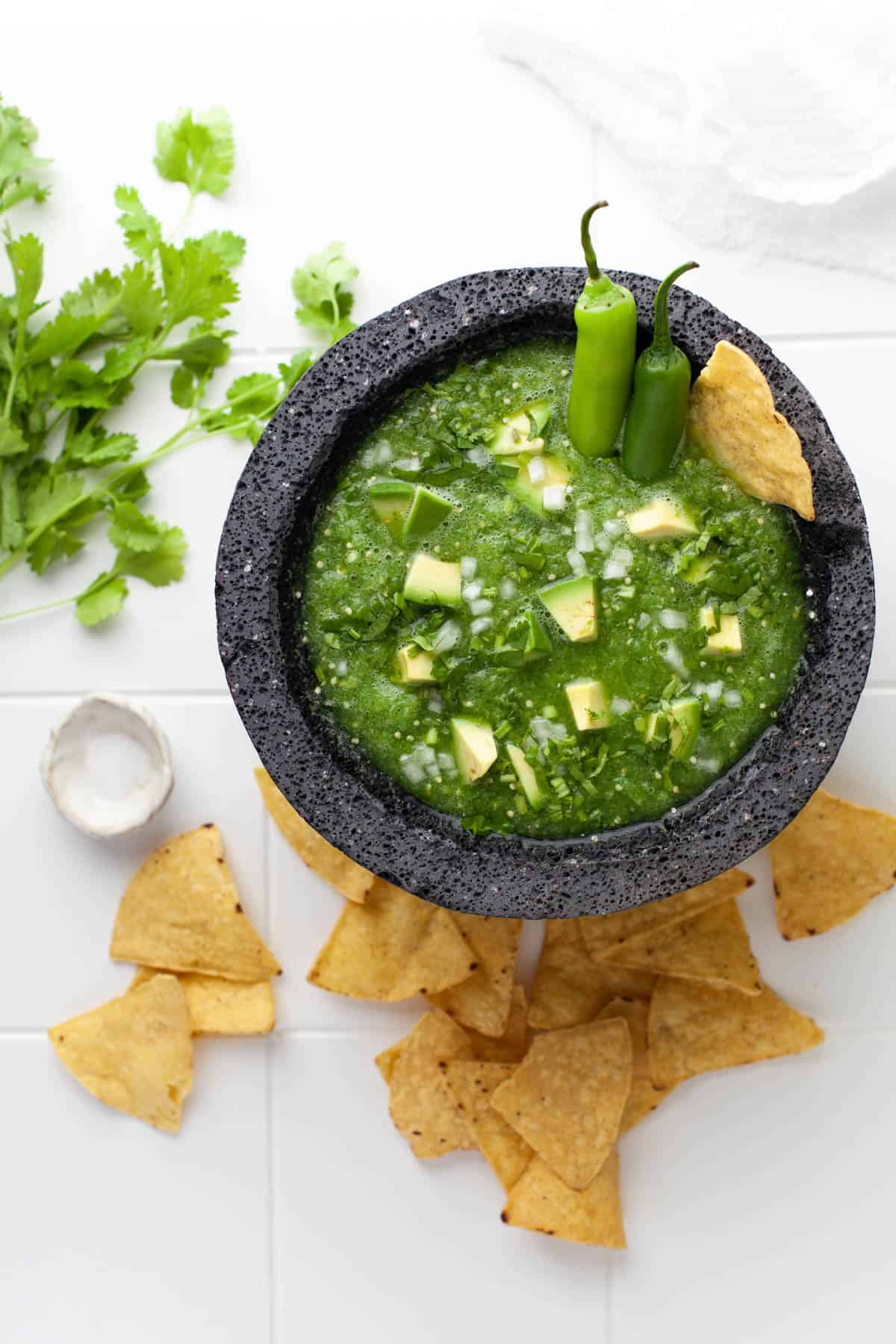 A molcajete filled with homemade salsa verde with chips and fresh cilantro beside it.