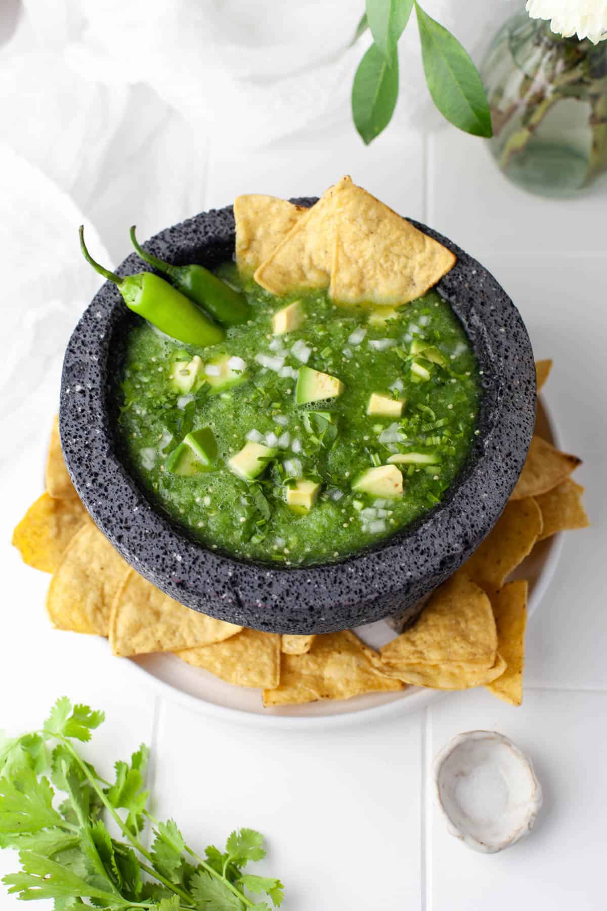 A bowl of tomatillo salsa verde surrounded by corn chips.
