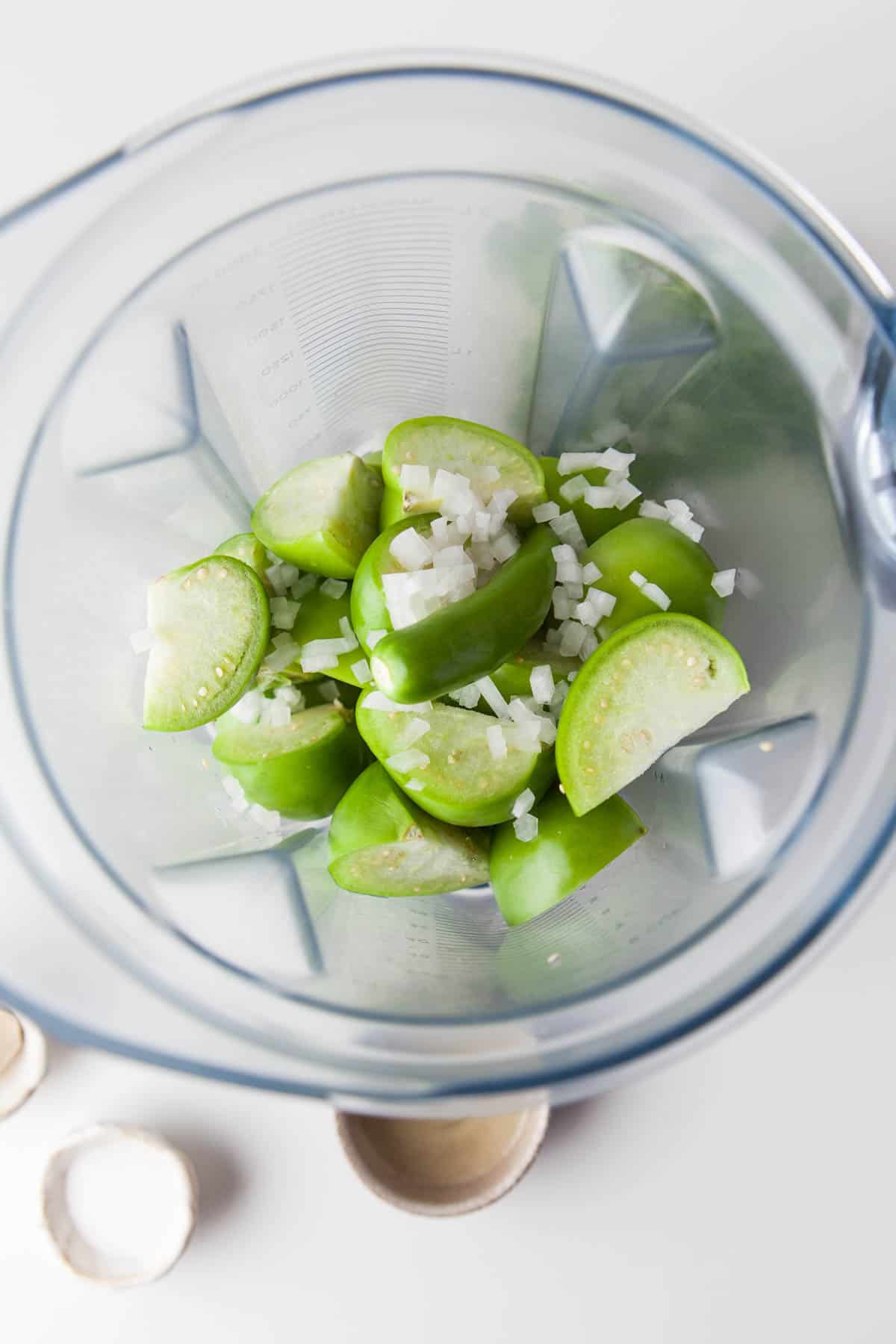Adding onion and jalapeno to tomatillos in a blender.