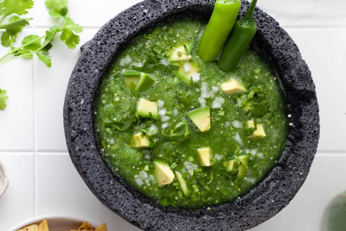 A large bowl of salsa verde garnished with chunks of avocado and jalapenos.
