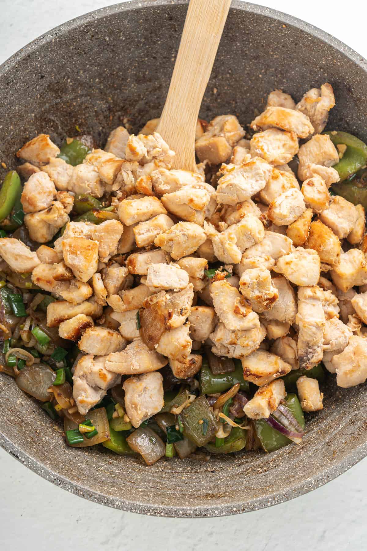 Adding cooked chicken pieces to softened vegetables.