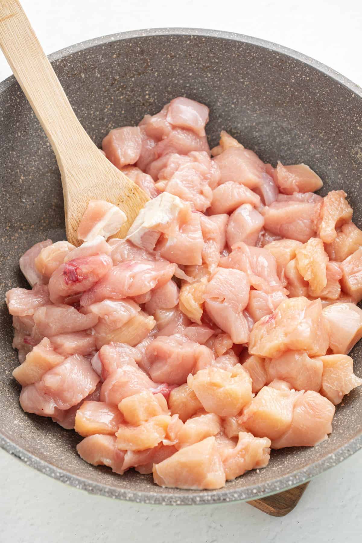 Stirring bite-size chunks of raw chicken in a pan with a spoon.