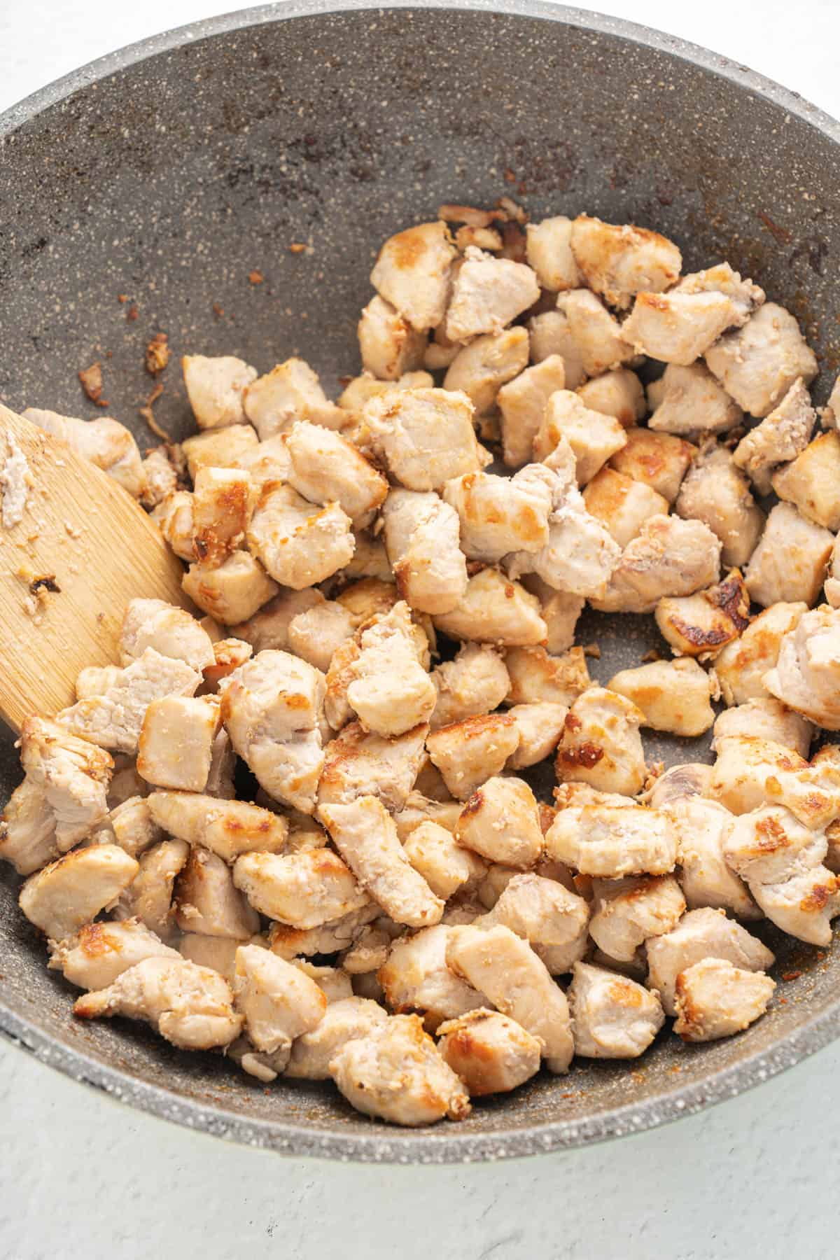 Cooked bite-size pieces of chicken breast in a pan.