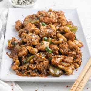 A large white plate of cashew chicken stir fry being served family style.