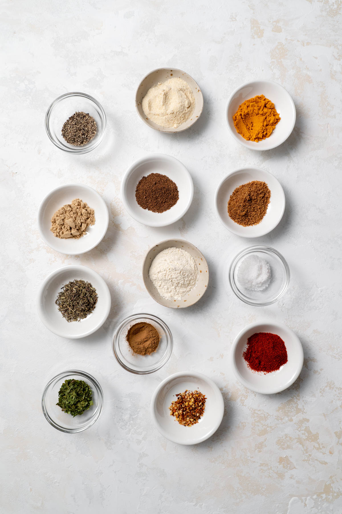 Overhead view of individual bowls filled with spices and arranged in a cluster. 