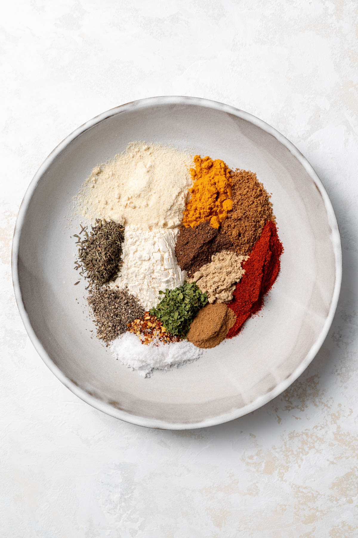 A shallow plate is filled with spices that have been grouped together before blending. 