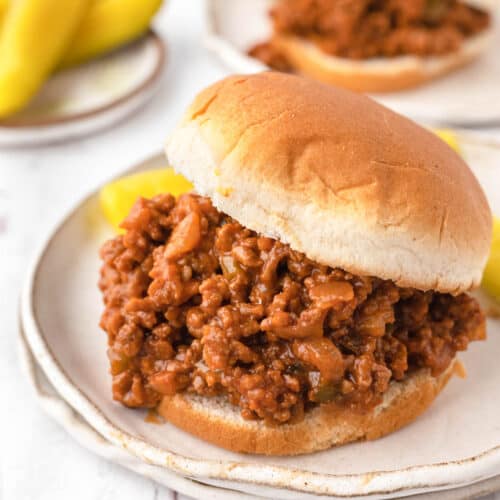 An image of sloppy joes on plates with pickles.