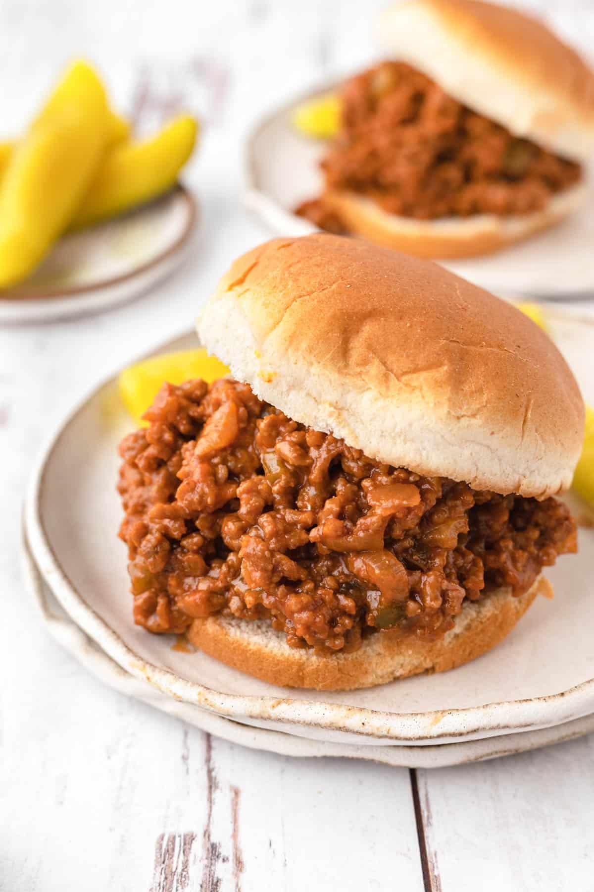 An image of sloppy joes on plates with pickles.