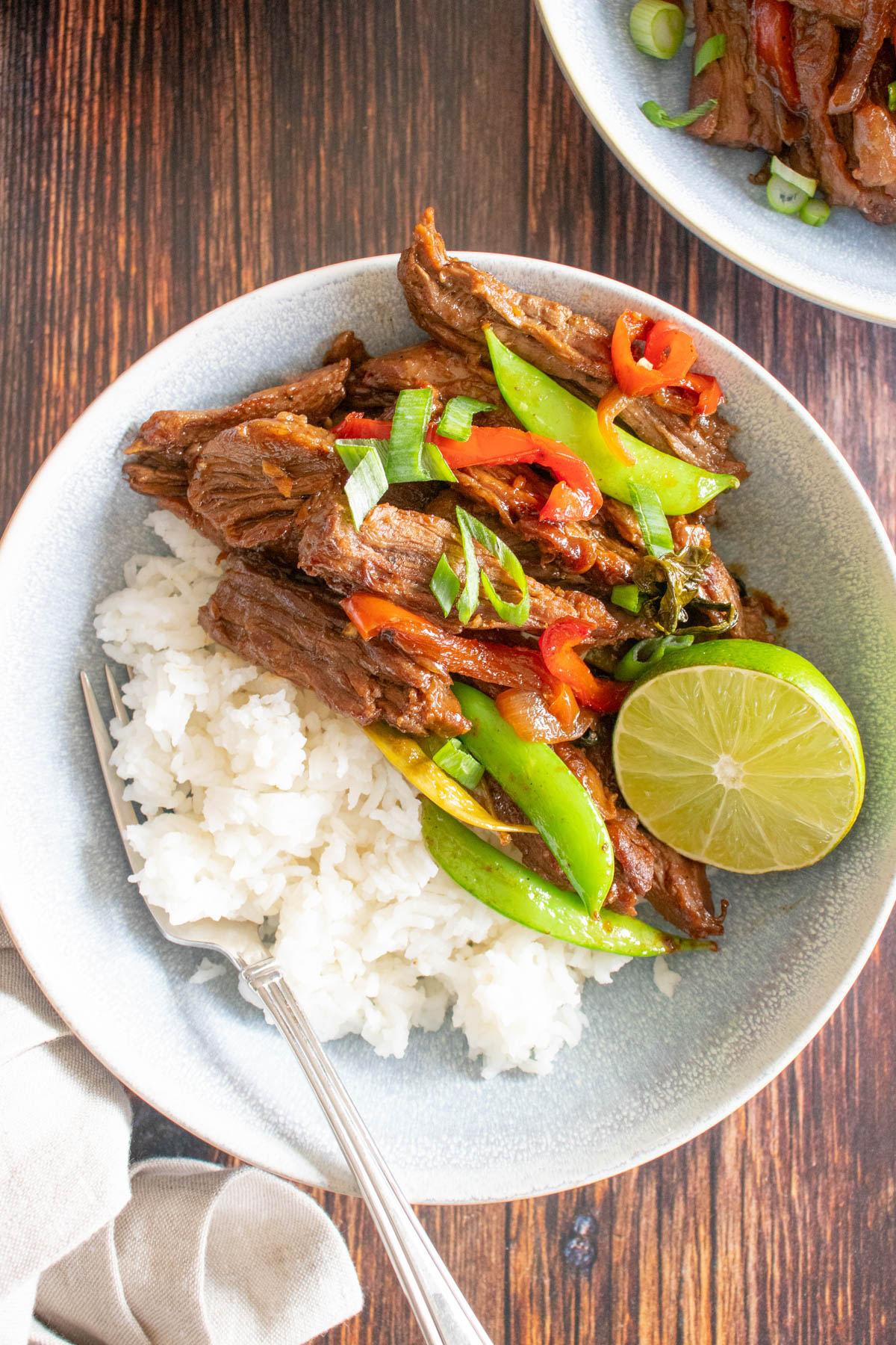 Overhead image of beef, vegetables, white rice and a lime in a bowl with a fork. 