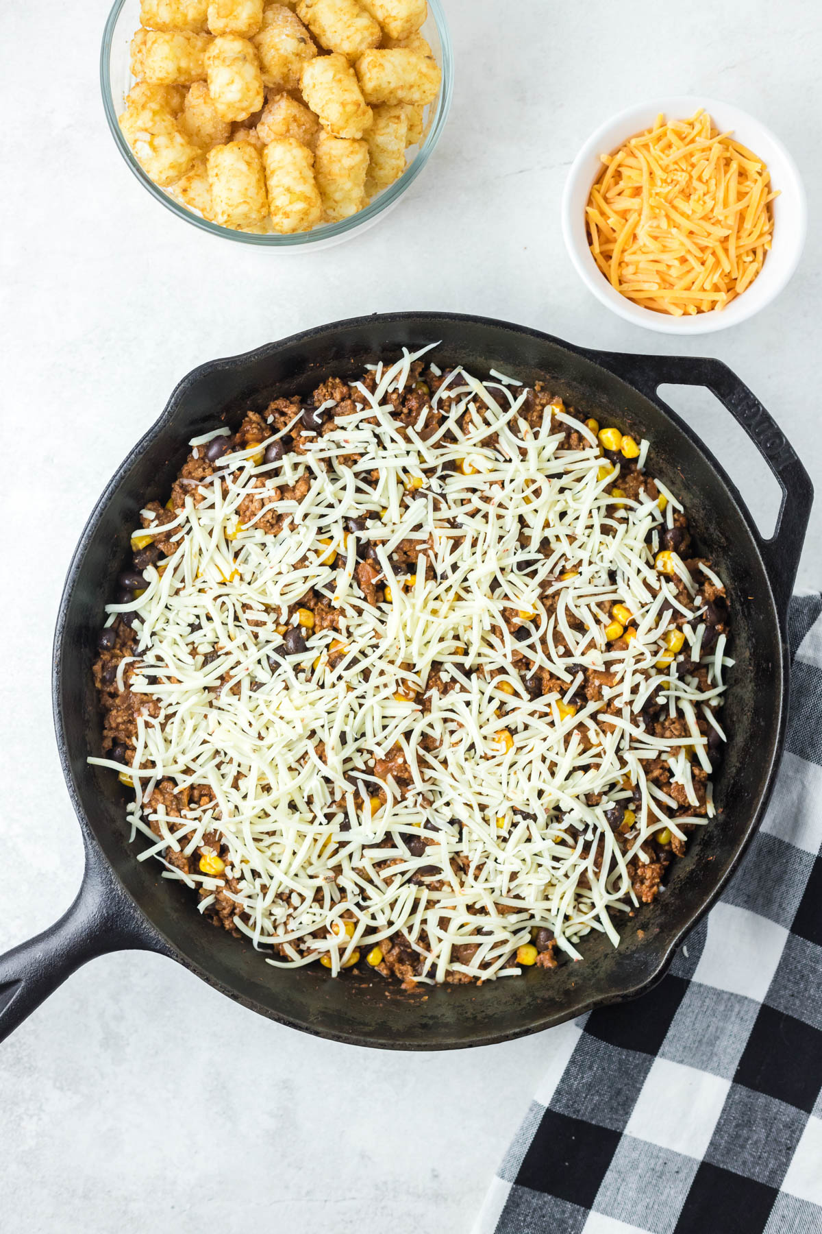 A ground beef mixture is topped with shredded cheese, in a skillet.