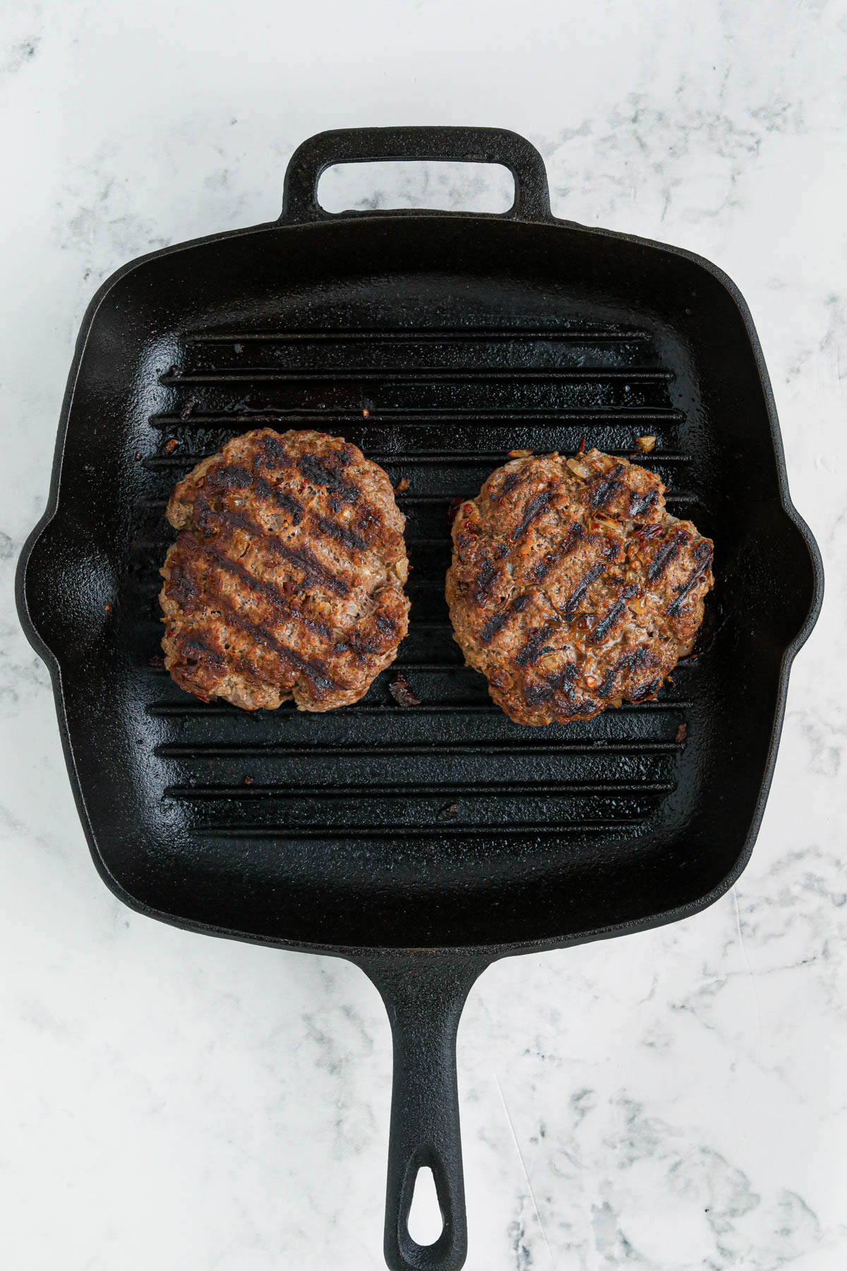 Overhead image of a black skillet with two cooked hamburgers. 