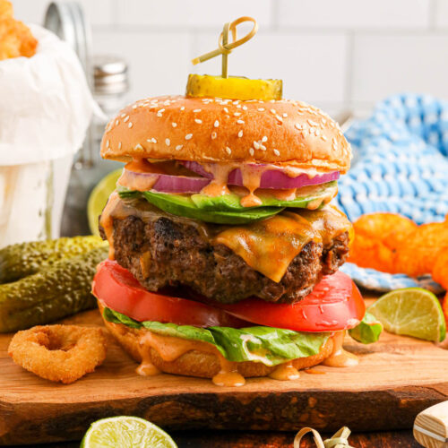 Chipotle burger on a wooden cutting board, with condiments visible around the burger in the foreground and background.