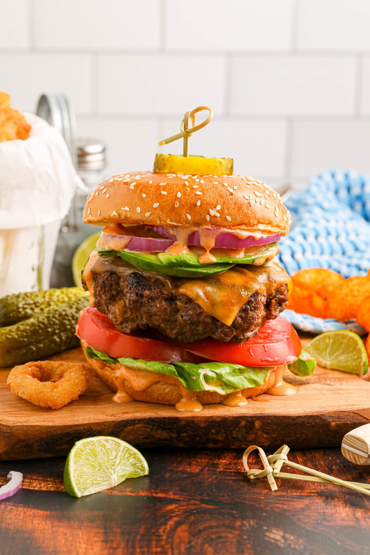 Chipotle burger on a wooden cutting board, with condiments visible around the burger in the foreground and background. 
