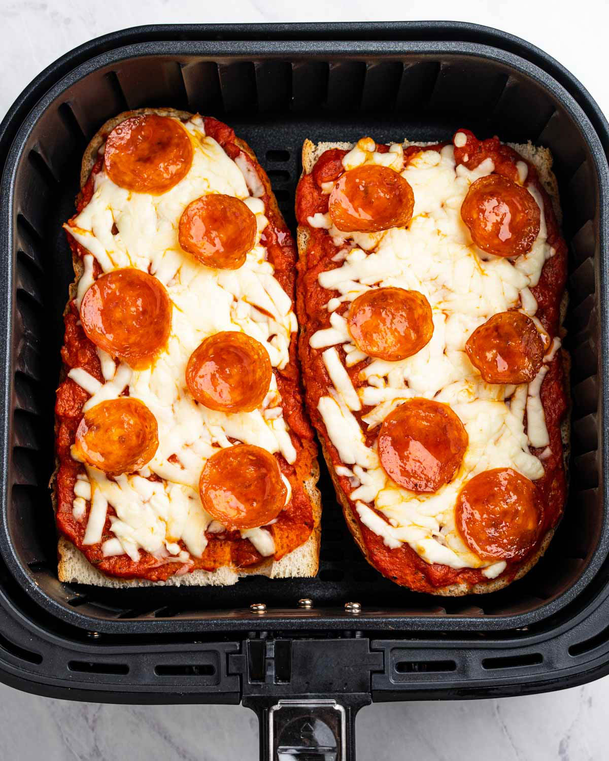 An air fryer is displayed, containing two cooked French bread pizzas. 