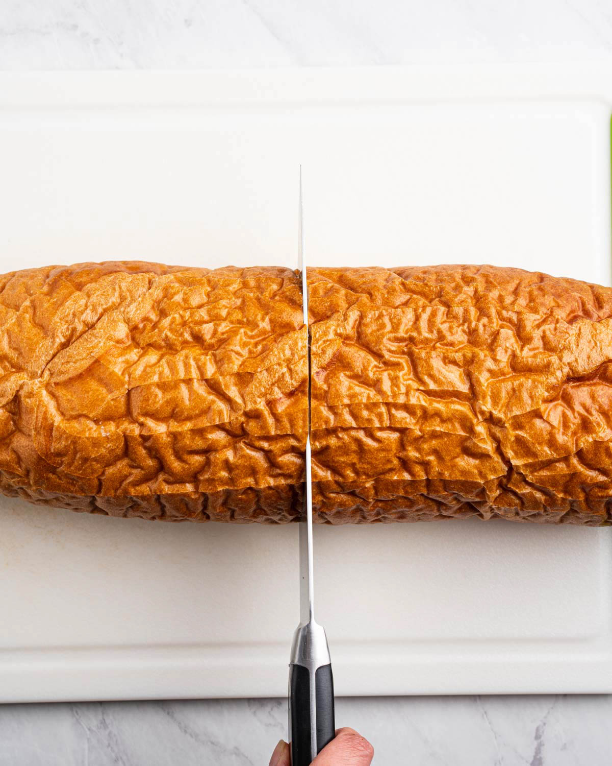 A loaf of french bread is being cut in half with a kitchen knife. 