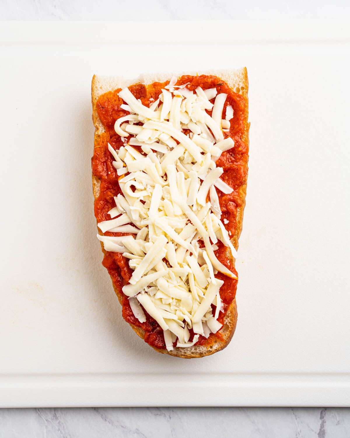 A french bread pizza has pizza sauce and shredded mozzarella cheese. 