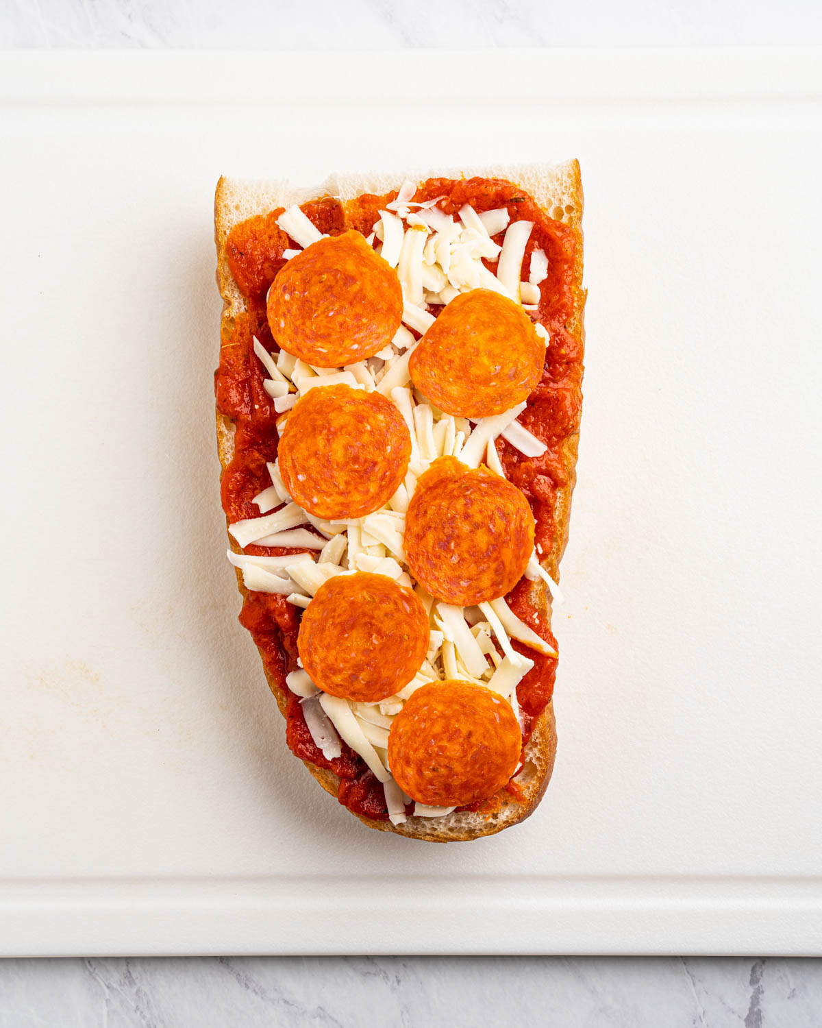 A slice of french bread is topped with pizza sauce, shredded mozzarella cheese and sliced pepperoni. 