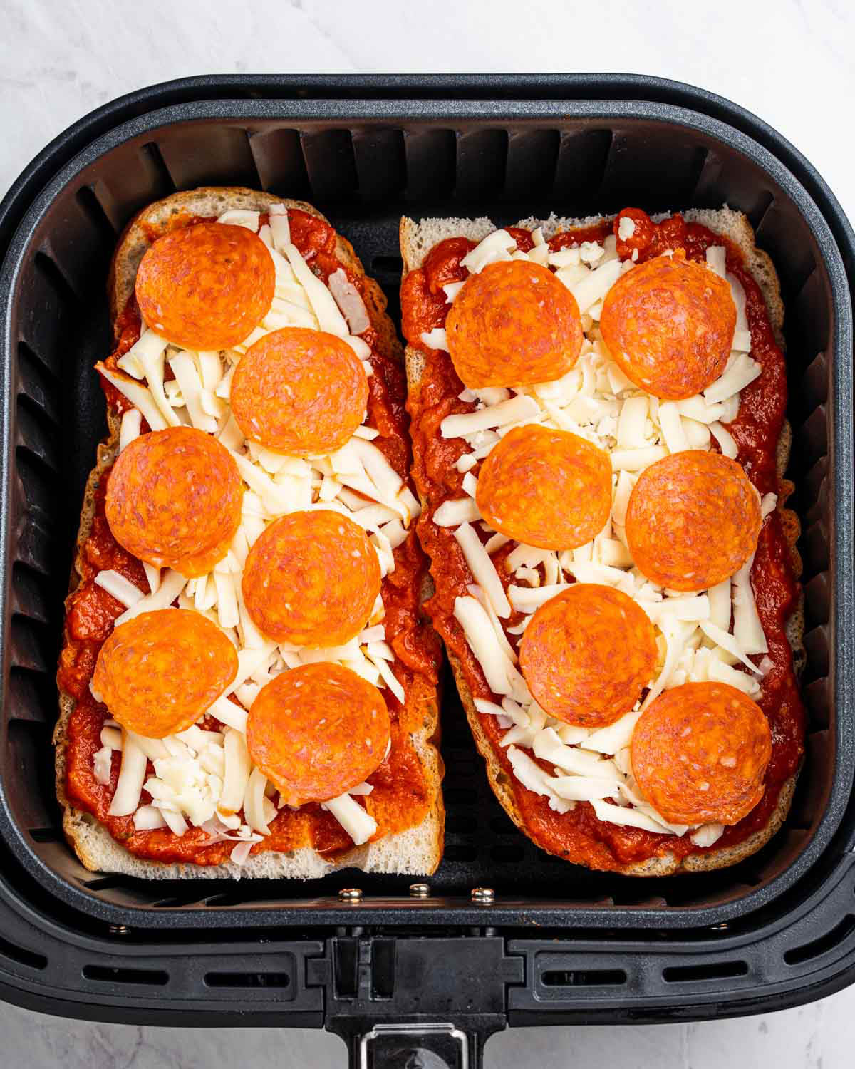 Two uncooked french bread pizzas are situated in an air fryer. 